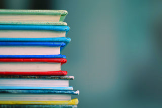 A stack of colourful books (red, blue, yellow and green) sit in front of a light blue background.