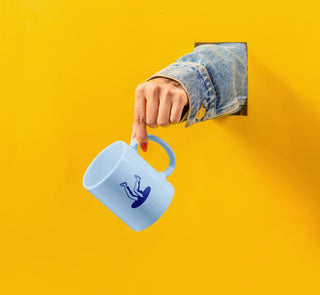 In a bright yellow wall, a hand in a denim jacket pokes through holding a light blue mug with a deep blue Parallel brand icon on it.