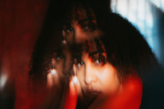 A woman has been photographed using a refracting filter. her curly hair sits in front of a red and blue background, her face mirrored above her