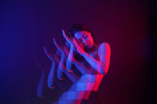 A woman stands in front of a dark background. through lighting effects and a reflecting filter, she has been duplicated several times with red and blue lighting glowing over her.